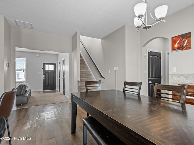 dining space with visible vents, stairs, hardwood / wood-style flooring, arched walkways, and a notable chandelier