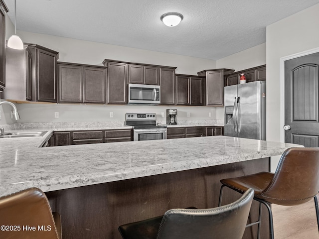 kitchen featuring dark brown cabinetry, stainless steel appliances, light countertops, and a sink