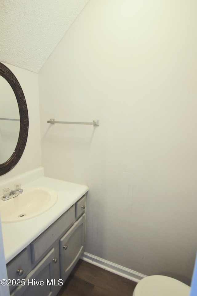 bathroom with toilet, a textured ceiling, wood finished floors, baseboards, and vanity