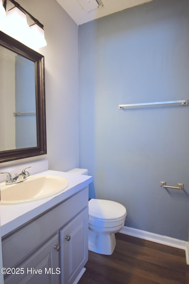 bathroom featuring baseboards, toilet, wood finished floors, and vanity