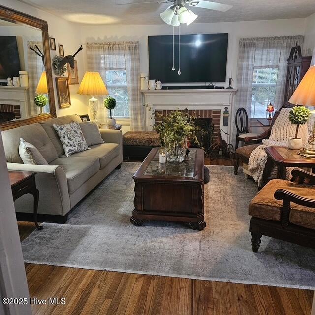 living area with a brick fireplace, a ceiling fan, and wood finished floors