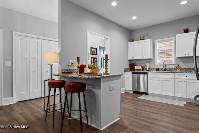 kitchen featuring stainless steel dishwasher, a kitchen breakfast bar, dark wood finished floors, and white cabinets