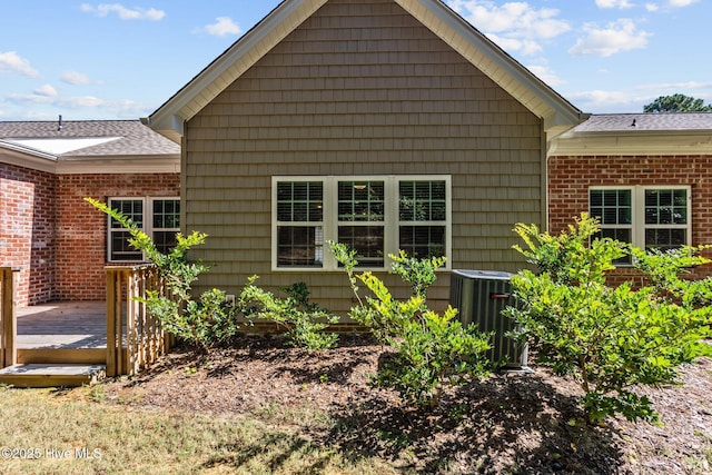 exterior space with a wooden deck, cooling unit, a shingled roof, and brick siding