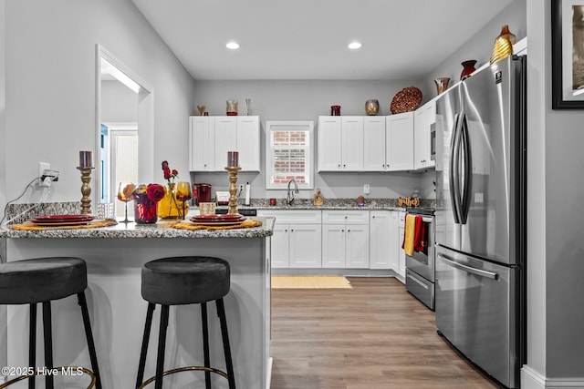 kitchen featuring a kitchen breakfast bar, appliances with stainless steel finishes, a peninsula, and white cabinets