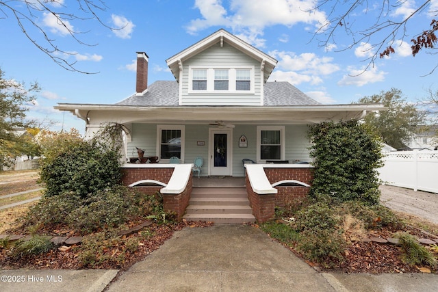 bungalow with covered porch, a chimney, roof with shingles, and fence