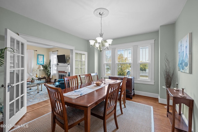 dining area with an inviting chandelier, a fireplace, baseboards, and light wood-style floors