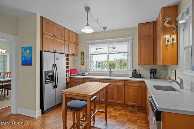 kitchen with a sink, stainless steel appliances, brown cabinets, and hanging light fixtures