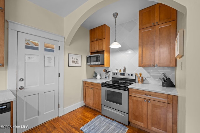 kitchen featuring stainless steel appliances, decorative backsplash, dark wood-type flooring, decorative light fixtures, and brown cabinets