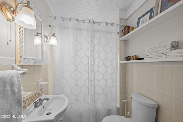 bathroom featuring shower / bath combo with shower curtain, toilet, tile walls, and a sink