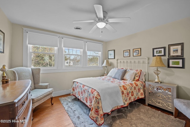 bedroom featuring a ceiling fan, wood finished floors, visible vents, and baseboards