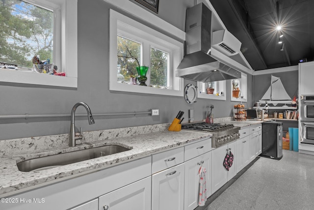 kitchen with a sink, white cabinetry, appliances with stainless steel finishes, wall chimney range hood, and light stone countertops