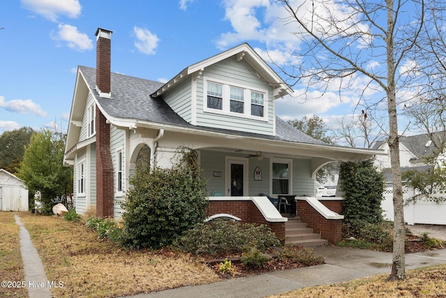 bungalow-style home featuring ceiling fan, a porch, roof with shingles, and a chimney