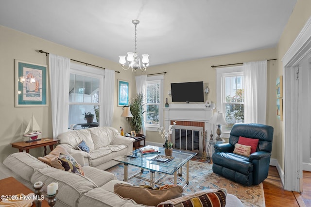 living room with a brick fireplace, baseboards, an inviting chandelier, and wood finished floors