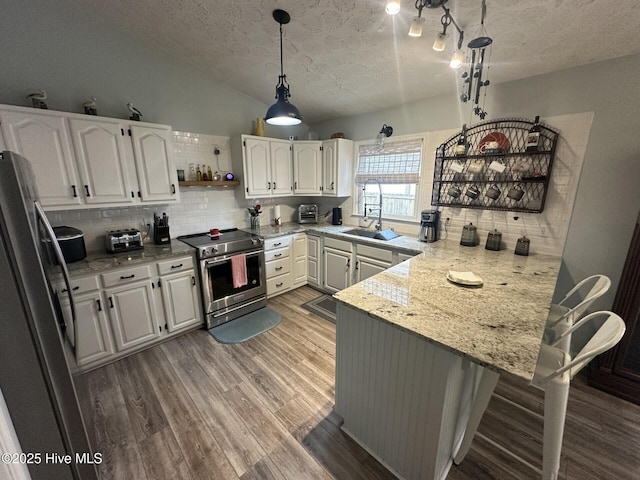 kitchen with a peninsula, white cabinetry, appliances with stainless steel finishes, and wood finished floors