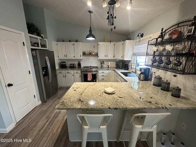 kitchen with light stone counters, a peninsula, vaulted ceiling, appliances with stainless steel finishes, and open shelves