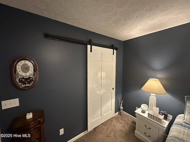 bedroom featuring a textured ceiling, dark colored carpet, a barn door, and baseboards