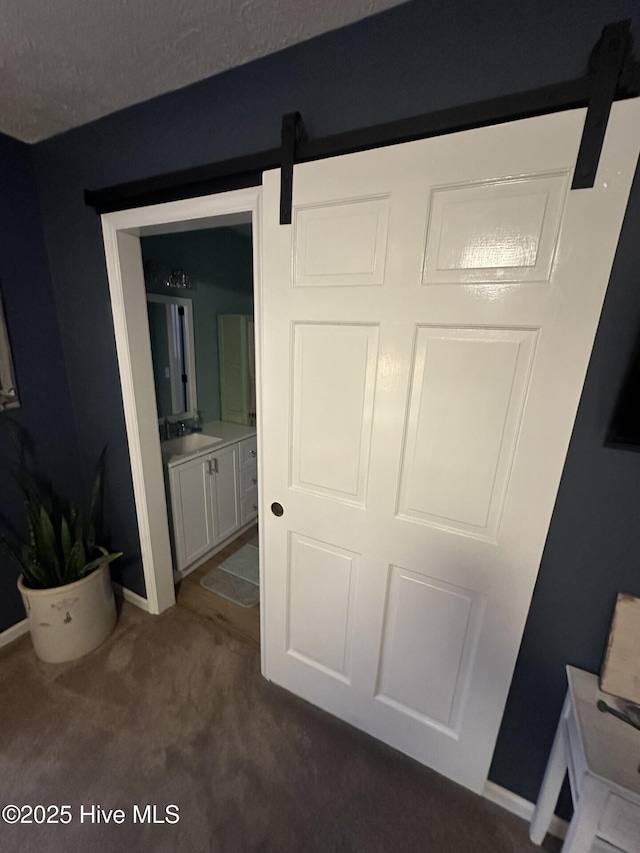 interior space with a barn door, baseboards, dark colored carpet, and a sink