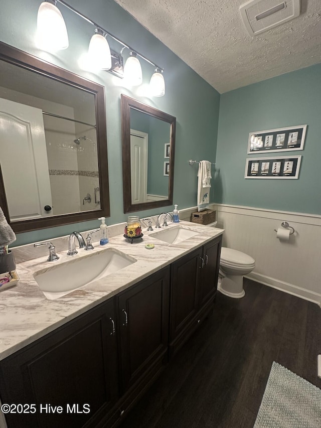 bathroom featuring a wainscoted wall, a sink, toilet, and wood finished floors