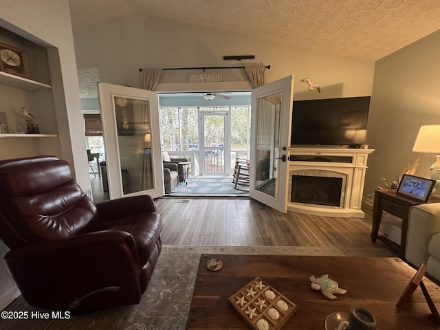 living area featuring a fireplace with raised hearth, vaulted ceiling, a textured ceiling, and wood finished floors