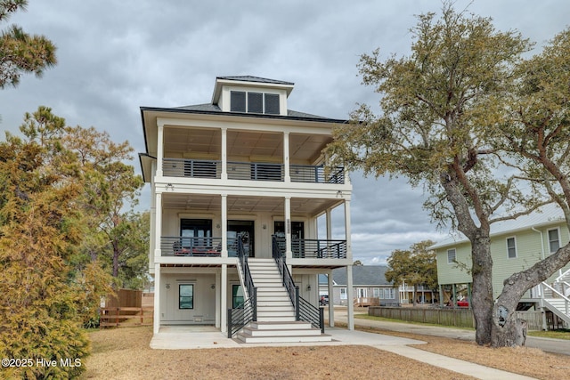 coastal home featuring stairway, a balcony, board and batten siding, and fence