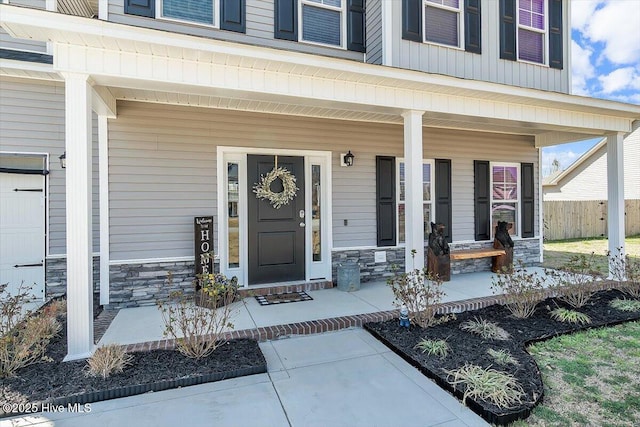 doorway to property featuring stone siding, covered porch, and fence