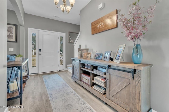 foyer with visible vents, light wood-style flooring, and an inviting chandelier