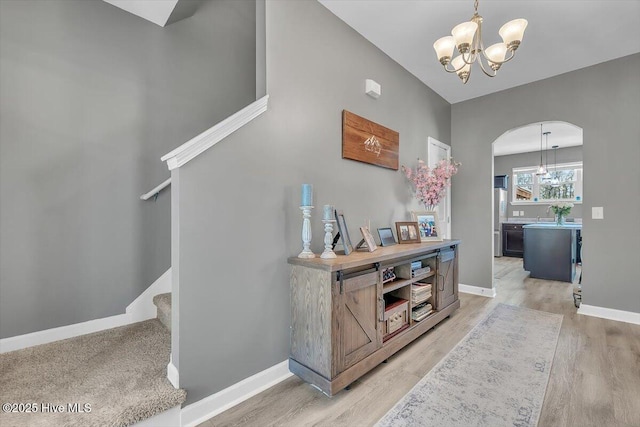 interior space with baseboards, stairway, light wood-type flooring, arched walkways, and a notable chandelier