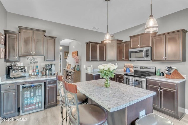 kitchen featuring visible vents, beverage cooler, appliances with stainless steel finishes, light wood-style floors, and arched walkways