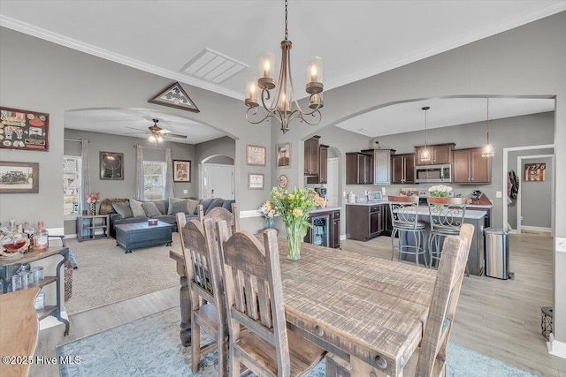 dining room with ceiling fan with notable chandelier, arched walkways, crown molding, light wood finished floors, and baseboards