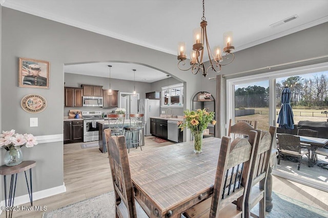 dining space featuring visible vents, arched walkways, ornamental molding, light wood-type flooring, and a wealth of natural light