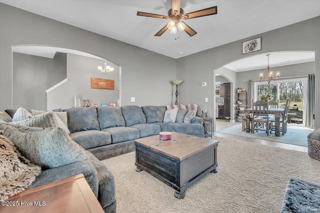 carpeted living room featuring arched walkways and ceiling fan with notable chandelier