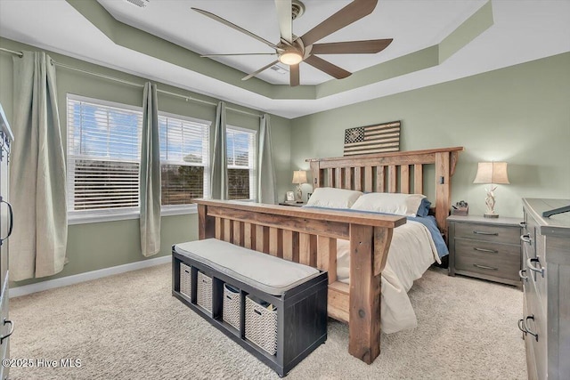 bedroom featuring light colored carpet, baseboards, a tray ceiling, and ceiling fan