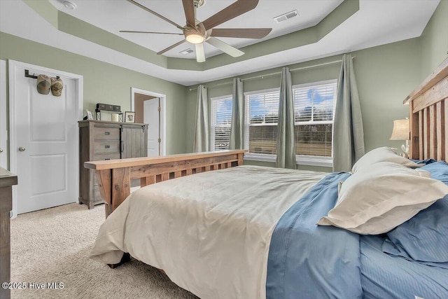 bedroom with ceiling fan, a tray ceiling, visible vents, and light carpet