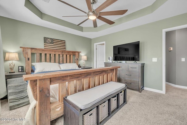 bedroom with light carpet, ceiling fan, baseboards, and a tray ceiling