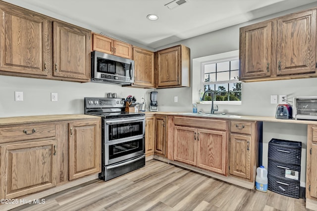 kitchen featuring visible vents, a sink, stainless steel appliances, light wood finished floors, and light countertops