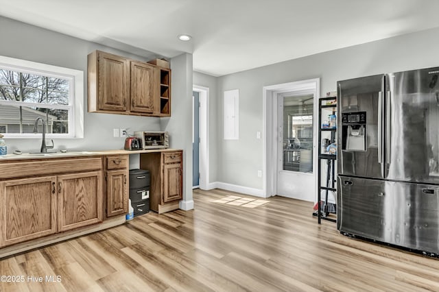 kitchen featuring light wood-style flooring, stainless steel refrigerator with ice dispenser, a sink, light countertops, and baseboards