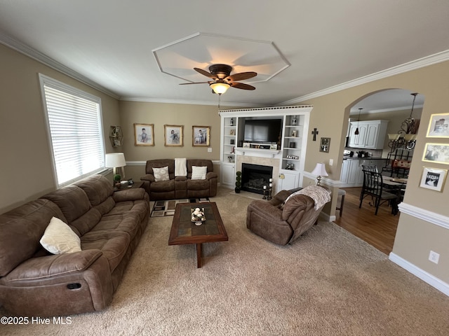 6725 Hemlock Ct, Sims, NC 27880 - living room featuring carpet flooring, arched walkways, a tiled fireplace, a ceiling fan, and crown molding