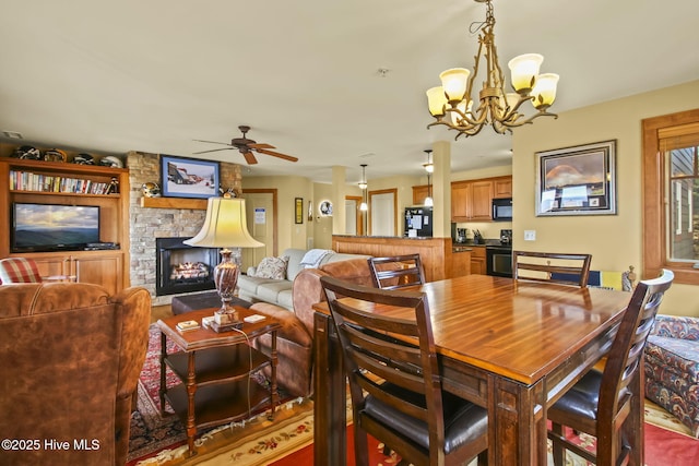 dining area featuring a stone fireplace and ceiling fan with notable chandelier