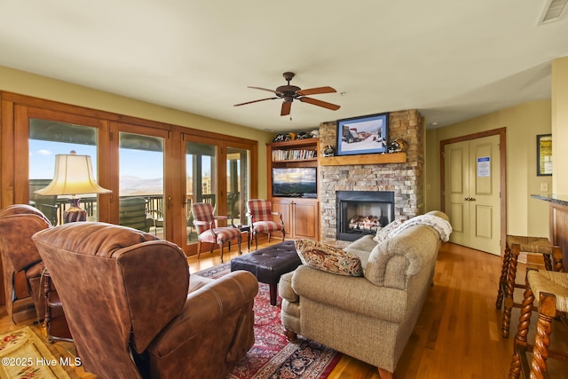 living area with visible vents, a stone fireplace, a ceiling fan, and wood finished floors