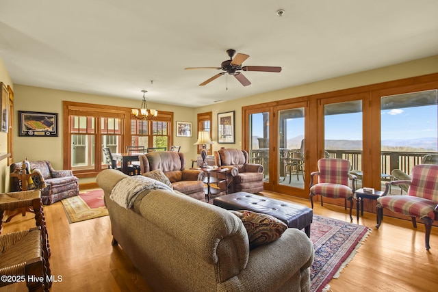 living room with ceiling fan with notable chandelier, light wood-type flooring, and a wealth of natural light