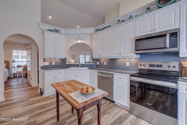 kitchen with arched walkways, white cabinets, appliances with stainless steel finishes, and a sink