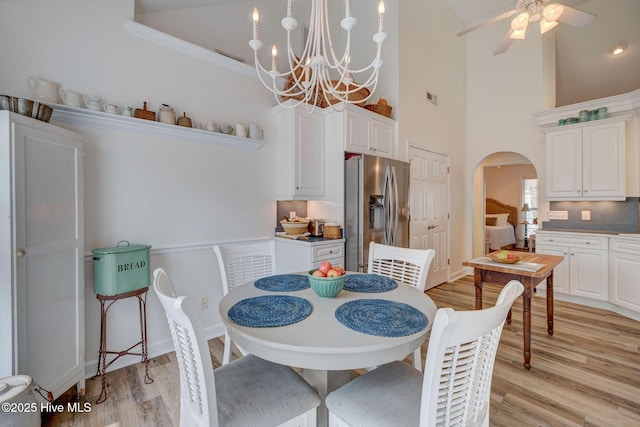 dining room with light wood finished floors, visible vents, ceiling fan with notable chandelier, a high ceiling, and arched walkways