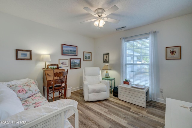 living area featuring visible vents, baseboards, ceiling fan, wood finished floors, and a textured ceiling