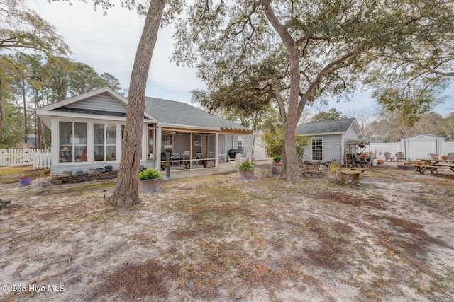 rear view of property featuring a patio area, a shingled roof, an outdoor structure, and fence