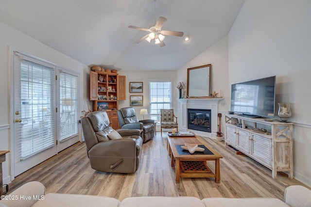 living area featuring high vaulted ceiling, a glass covered fireplace, a ceiling fan, and light wood finished floors