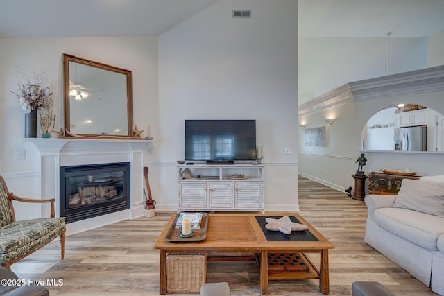 living room featuring visible vents, ceiling fan, light wood-style floors, a glass covered fireplace, and high vaulted ceiling