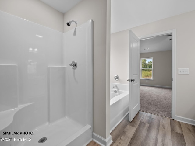 full bath with a garden tub, wood finished floors, baseboards, and walk in shower