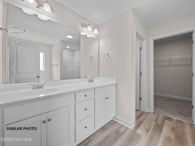 full bathroom with double vanity, a spacious closet, wood finished floors, and a sink