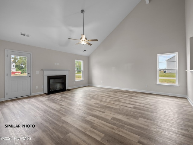 unfurnished living room with a glass covered fireplace, high vaulted ceiling, baseboards, and wood finished floors