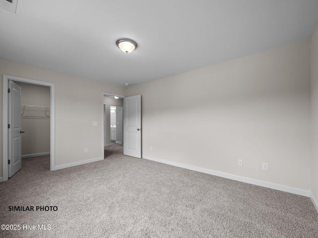 unfurnished bedroom with a walk in closet, visible vents, a closet, carpet flooring, and baseboards